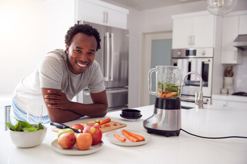 Fototapeta na wymiar Portrait Of Man Wearing Pyjamas Standing In Kitchen Chopping Fruit And Vegetables For Fresh Smoothie