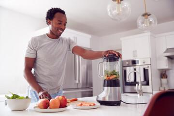 Fototapeta na wymiar Man Wearing Pyjamas Standing In Kitchen Putting Fresh Fruit And Vegetables Into Blender