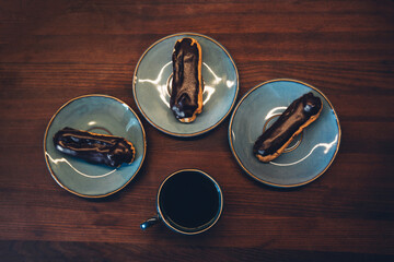 Chocolate eclairs and coffee cup on dark wooden background.