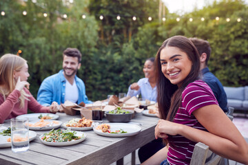 Portrait Of Woman With Friends At Home Sitting At Table Enjoying Food At Summer Garden Party
