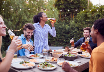 Multi-Cultural Friends At Home Around Table Drinking Beer As They Enjoy Food At Summer Garden Party