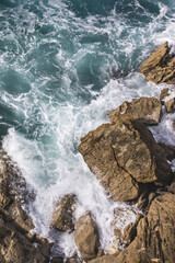 Bay of Biscay. Raging force of nature. Waves lick stones and beat against rocks. Spanish coast. Salty sea air. Boulders and stones in the spray of sea waves. Seascape view from above. Frosty breeze. 
