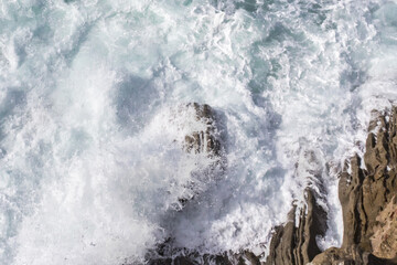 Fototapeta na wymiar Bay of Biscay. Raging force of nature. Waves lick stones and beat against rocks. Spanish coast. Salty sea air. Boulders and stones in the spray of sea waves. Seascape view from above. Frosty breeze. 