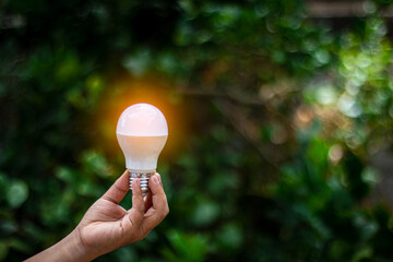 Hand holding a light bulbs on green blur backgroud, idea solar energy in nature.