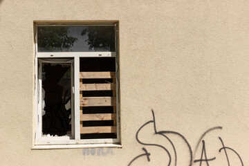 A building with a broken boarded up window. Vandalism, graffiti