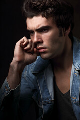 Handsome serious thinking male model posing in fashion blue jeans jacket looking on dark shadow background. Closeup