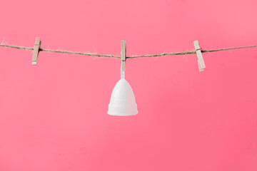 Menstrual cup white eco friendly hanging on clothesline isolated on pink background, photo for women's blog or ad poster