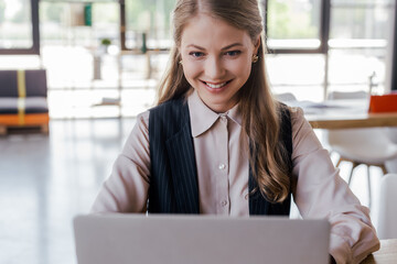 selective focus of happy businesswoman using laptop in office