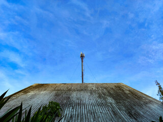 The pole stands tall on the roof of the house. With a blue sky as a background