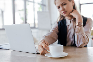 selective focus of businesswoman touching cup of coffee near laptop