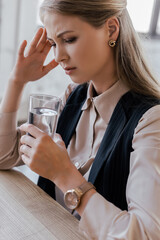 tired businesswoman having headache and holding glass of water