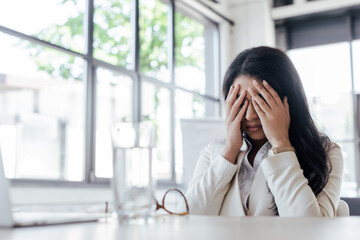 selective focus of tired businesswoman covering face near glass of water on table