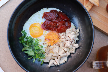 pan fried egg with toppings, Chinese sausage and pork sausage in the black pan.