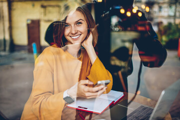 Half length portrait of happy beautiful blogger received good comments from followers under last publication in own website.positive student updating application on smartphone smiling at camera