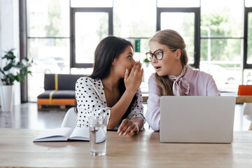 businesswomen gossiping near laptop in modern office