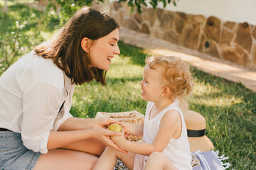 Young mother and her child having cozy summer picnic with fresh lemonade and fruits in a park.