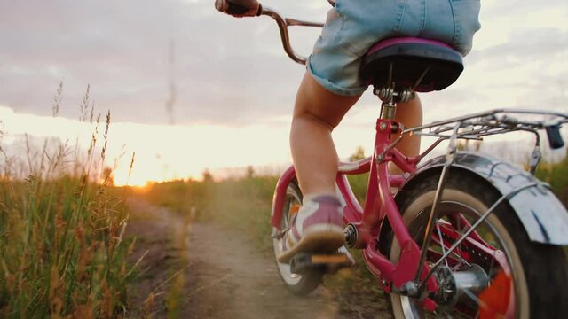 Little girl riding bike on meadow trail at sunset, to pedal close up