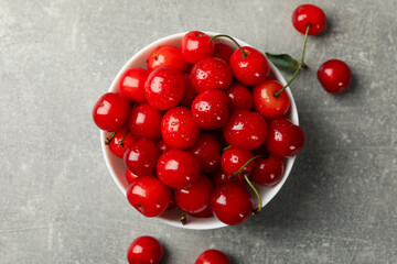 Bowl with red cherry on gray background, top view