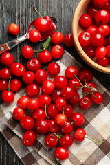 Towel, spoon and bowl with cherry on wooden background, top view