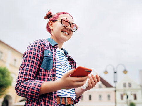 Smiling beautiful modern young female teenager Portrait with extraordinary hairstyle in checkered shirt holding a slim smartphone in hand. Modern teens or cheerful students concept image.