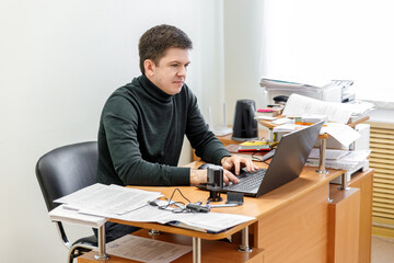 A casual businessman works in an office, sits at a Desk, types on a keyboard, looks at a computer screen. Concept of office work.