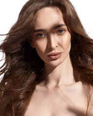 Beautiful young brunette with natural make-up and silk long hair on a white background. Shadow on the face. Woman looking at camera. Isolated over white background.