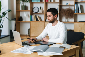Fototapeta premium Photo of focused bearded man working with laptop and digital tablet