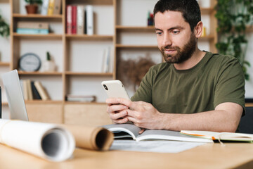 Photo of man using smartphone while working with drawings and laptop