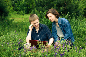 Attractive happy smiling young lesbian couple with laptop outdoors; outdoor office or social distancing concept