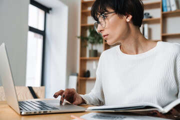 Image of focused woman working with laptop while sitting at table