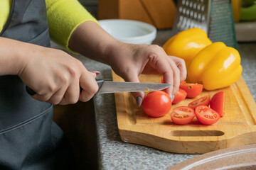Close up view of female cook slices cherry tomatoes on wooden board colorful vegetables on background, woman cooking fresh low-calorie salad in kitchen. Healthy food, diet, organic farm products