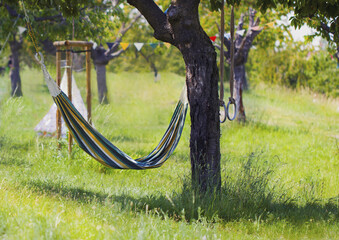 A striped hanging hammock and children's sports rings on a tree in the Park.Colored flags and a children's tent.The concept of entertainment and recreation in the fresh air on a Sunny summer day