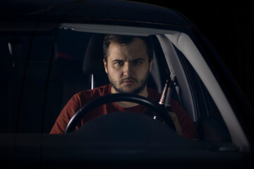 Portrait of Handsome young man driver sits at steering wheel of car at night tired looking forward and holding glass bottle. safe driving concept. alcohol and driving concept. Loneliness Concept.