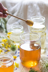 A honey jar with a spoon for honey in hand with flowers in background, selektive focus, backlight