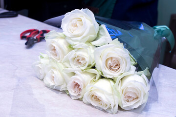Bouquet white roses are paper-wrapped in flower shop. Scissors and secateurs.