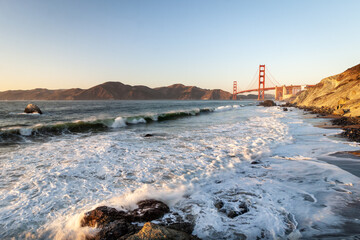 The evening view of Golden Gate Bridge with the waves of Atlantic Ocean in the foreground