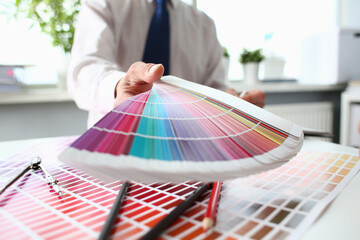 Cropped photo of male designer in suit holding catalogue palette guide at workplace for customer