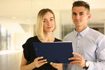 Waist up of smiling man and woman staying at workplace while holding document in hands. Business concept. Copy space
