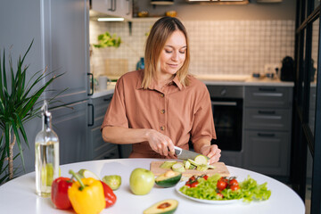 Obraz na płótnie Canvas Young smiling vegetarian woman preparing healthy vegan food alone at home. Attractive fit girl prepare healthy dinner, make surprise for husband. Healthy food lifestyle concept.