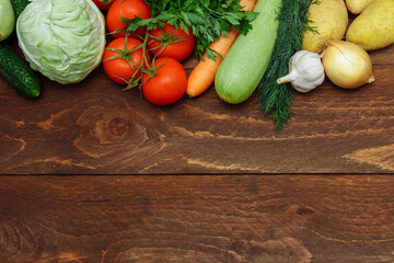 Raw vegetables cucumber, cabbage, tomatoes on a branch, carrots, zucchini, onions, garlic, potatoes and bunches of dill and parsley on a brown wooden background top view, the concept of healthy food