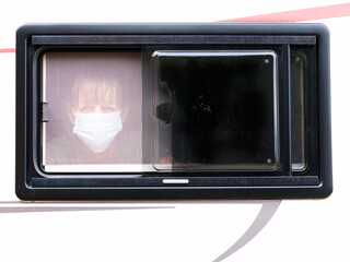 A lady wearing a face mask looks from behind the mosquito netting of her motorhome window.Coronavirus.Image