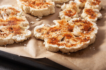 raw cauliflower steaks with spice on baking tray. plant based meat substitute