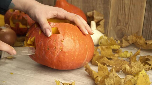 Woman removes pieces of pumpkin with knife to make mouth on it. Closeup of female hands carving the vegetable to make DIY jack-o-lantern. Theme of halloween and it's dreadful symbols.