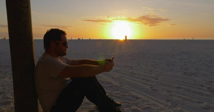 487 Man sitting on a beach during a sunset while on the phone