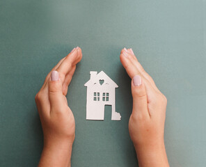 hands holding paper house cutout, on the  color background, family protection concept, property insurance