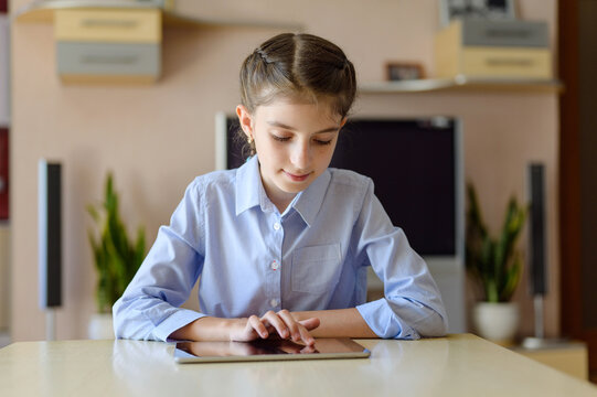girl sitting in a room at a table with a tablet. A girl moves her finger on the touch screen.