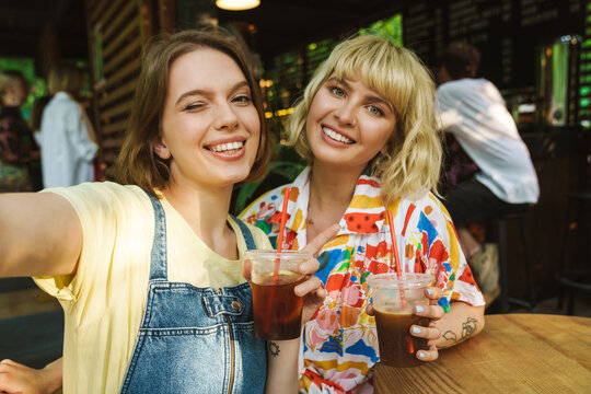 Image of two women taking selfie and winking while drinking soda