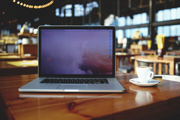 Open laptop computer and cup of coffee lying on a wooden table in cafe bar interior, portable net-book with copy space screen for your information content or text message, freelance work via internet