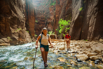 Group of diverse people hiking through a river at Zion National Park. Exploring the beauty of the Narrows and the beautiful canyons of southern Utah.