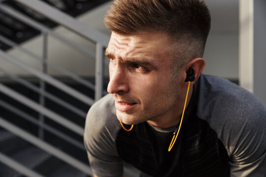 Image of young athletic sportsman using earphones while working out
